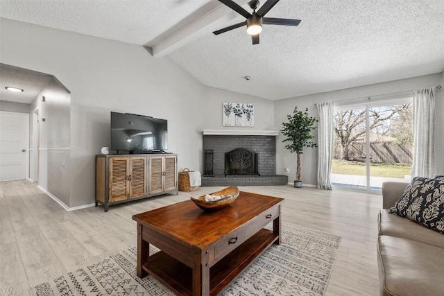 living area with vaulted ceiling with beams, a textured ceiling, a fireplace, and light wood-style flooring