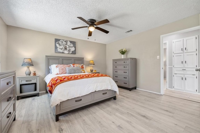 bedroom featuring baseboards, visible vents, ceiling fan, a textured ceiling, and light wood-style floors