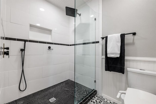 bathroom with wainscoting, a tile shower, and toilet