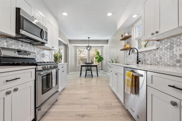 kitchen featuring light wood finished floors, a sink, stainless steel appliances, light countertops, and backsplash