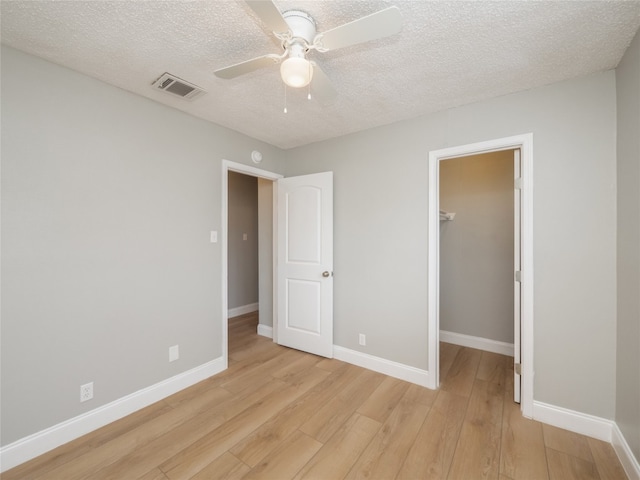 unfurnished bedroom featuring light wood-style flooring, a walk in closet, visible vents, and baseboards