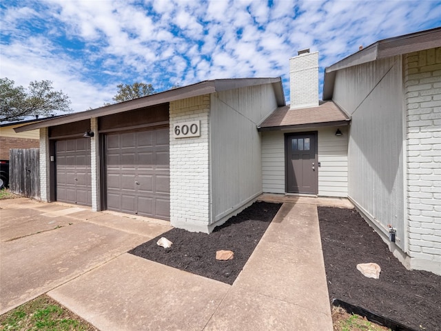 entrance to property with a garage, a chimney, and brick siding