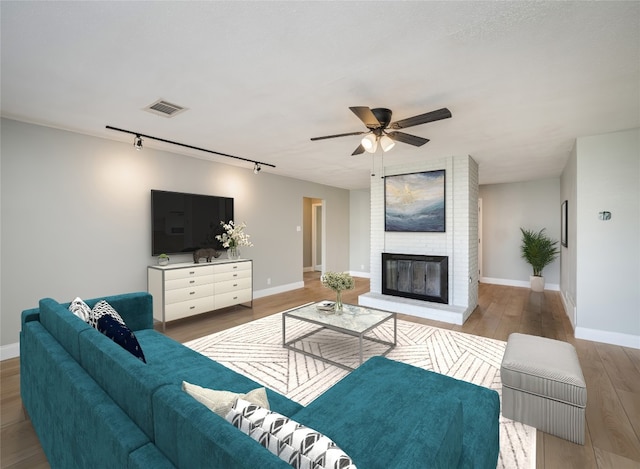 living room with a fireplace, visible vents, a ceiling fan, wood finished floors, and baseboards