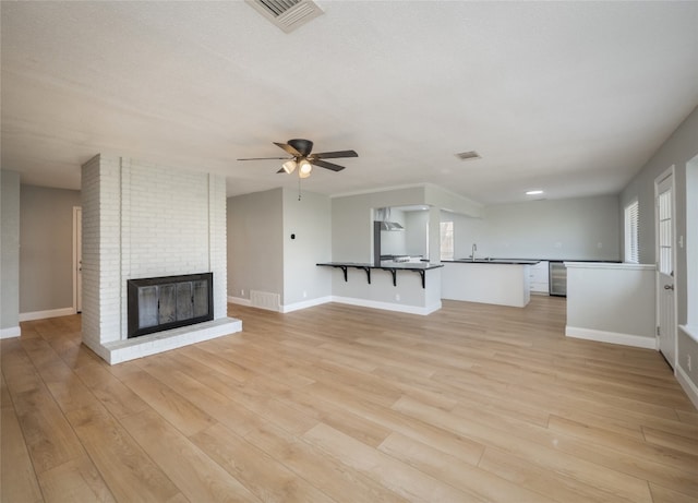 unfurnished living room with ceiling fan, a brick fireplace, visible vents, and light wood-style floors