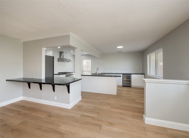 kitchen featuring light wood-style flooring, white cabinetry, a sink, beverage cooler, and wall chimney exhaust hood