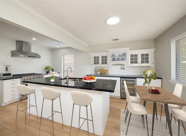 kitchen featuring wine cooler, a sink, wall chimney range hood, and dark countertops