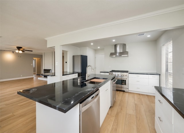 kitchen featuring stainless steel appliances, white cabinetry, a sink, light wood-type flooring, and wall chimney exhaust hood