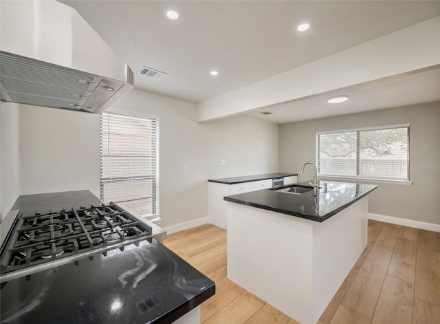 kitchen with visible vents, island range hood, white cabinets, light wood-type flooring, and a sink