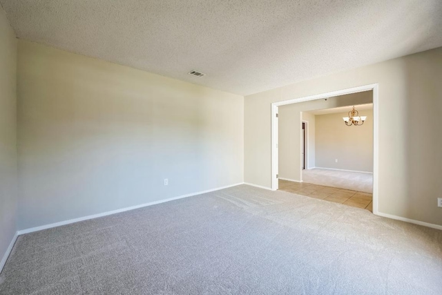 carpeted spare room featuring baseboards, visible vents, a textured ceiling, and an inviting chandelier