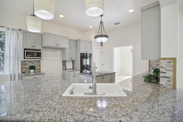 kitchen with light stone counters, decorative backsplash, stainless steel microwave, dobule oven black, and visible vents