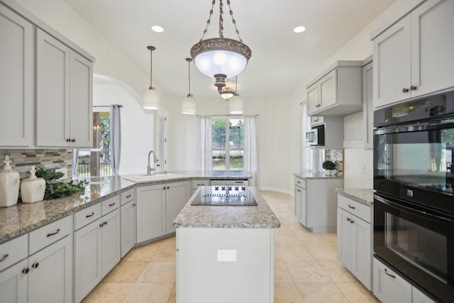 kitchen featuring a sink, black appliances, backsplash, a peninsula, and light stone counters