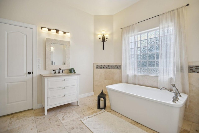 bathroom with a wainscoted wall, tile walls, a freestanding tub, and vanity