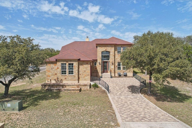 view of front of home with a chimney, a front yard, driveway, and stone siding
