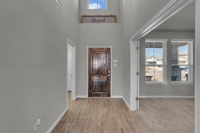 foyer entrance with a towering ceiling, baseboards, and wood finished floors