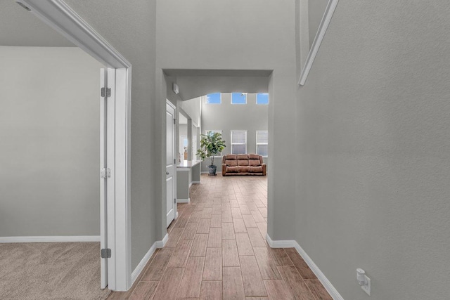 hallway featuring baseboards, a high ceiling, and wood finished floors