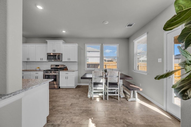 kitchen with white cabinets, appliances with stainless steel finishes, visible vents, and decorative backsplash