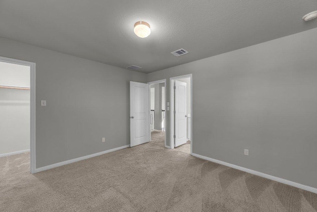 unfurnished bedroom featuring visible vents, baseboards, carpet, a spacious closet, and a textured ceiling