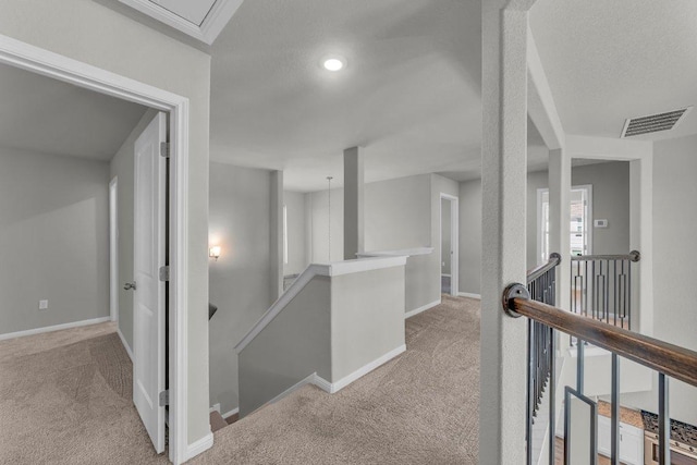 hallway featuring baseboards, visible vents, an upstairs landing, a textured ceiling, and carpet flooring