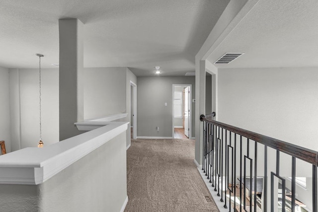 hallway featuring carpet flooring, visible vents, a textured ceiling, and an upstairs landing