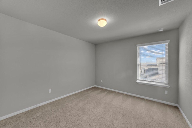 carpeted spare room featuring a textured ceiling and baseboards