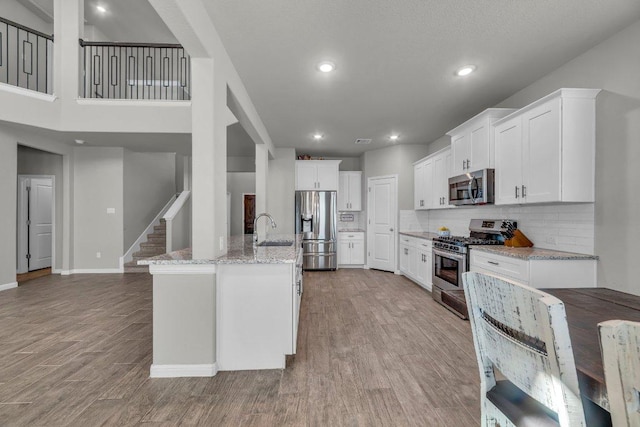 kitchen featuring tasteful backsplash, white cabinets, appliances with stainless steel finishes, wood finished floors, and light stone countertops