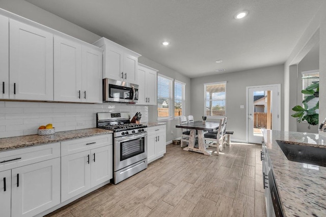 kitchen with stainless steel appliances, a sink, white cabinetry, light wood-type flooring, and decorative backsplash