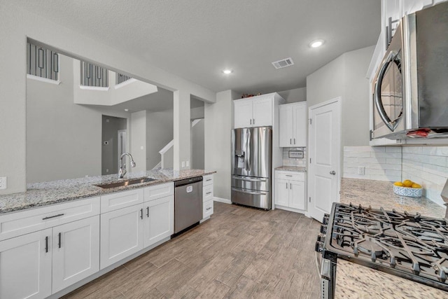 kitchen with light wood-style flooring, a sink, stainless steel appliances, white cabinetry, and backsplash