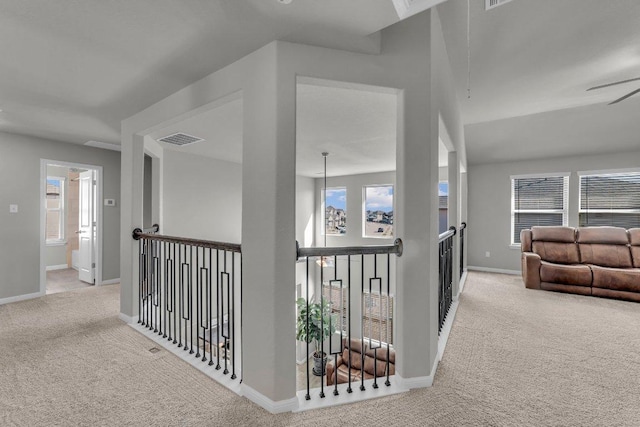 hallway featuring carpet, visible vents, baseboards, and an upstairs landing