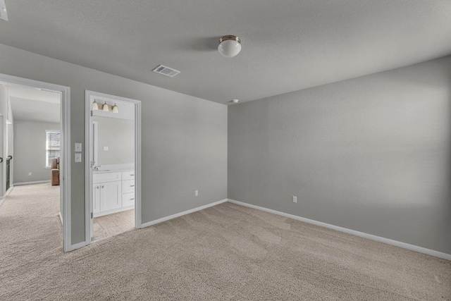 unfurnished bedroom with visible vents, light carpet, connected bathroom, a textured ceiling, and baseboards