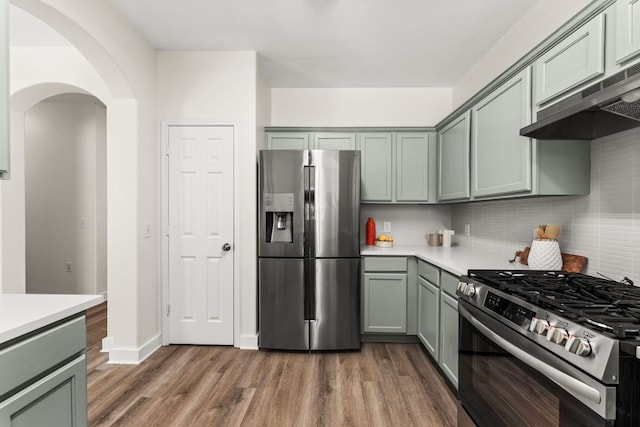 kitchen with arched walkways, appliances with stainless steel finishes, wood finished floors, and range hood