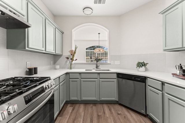 kitchen with dark wood-style floors, appliances with stainless steel finishes, gray cabinetry, under cabinet range hood, and a sink