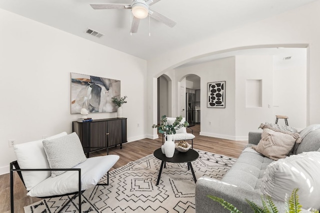 living room featuring arched walkways, visible vents, baseboards, and wood finished floors