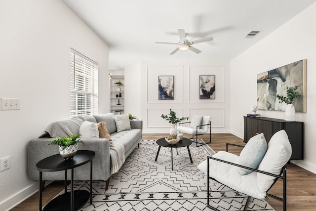 living room featuring a ceiling fan, visible vents, baseboards, and wood finished floors