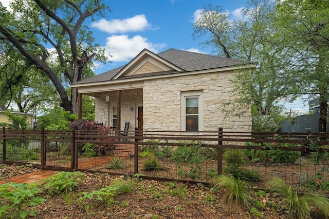 view of front of home with stone siding, a fenced front yard, and a shingled roof