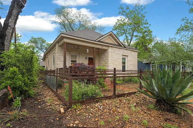 exterior space featuring stone siding, a shingled roof, and fence