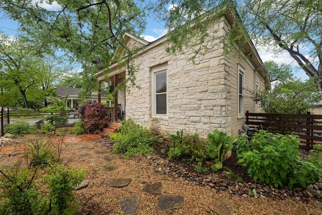 view of side of property with stone siding and fence