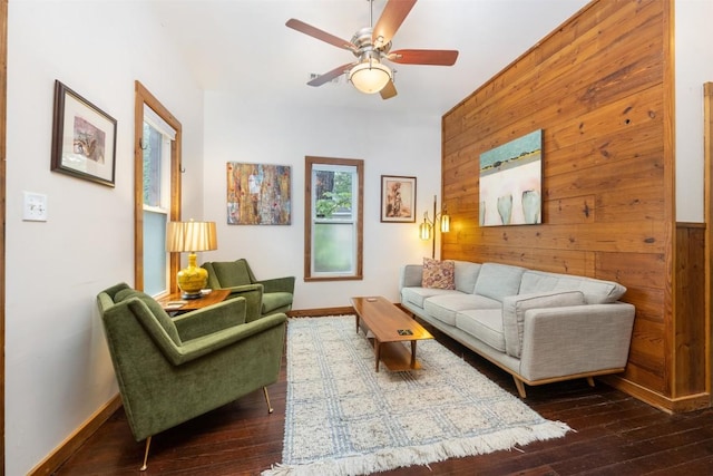 living room with dark wood-style flooring, wood walls, and ceiling fan