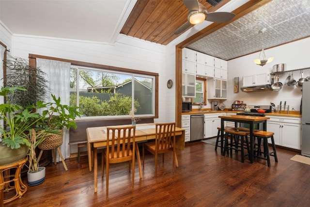 dining area with crown molding, wooden walls, a ceiling fan, and dark wood-style flooring