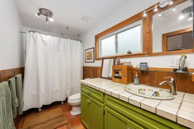 bathroom with vanity, wooden walls, visible vents, wainscoting, and toilet