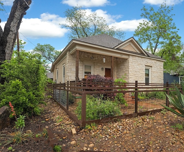 exterior space with a fenced front yard, stone siding, and roof with shingles