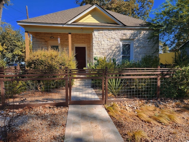 view of front of home featuring a fenced front yard, stone siding, roof with shingles, and a gate