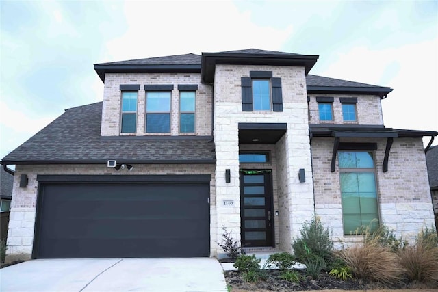 prairie-style home featuring driveway, stone siding, brick siding, and roof with shingles