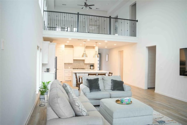 living area featuring a ceiling fan, a high ceiling, light wood-style flooring, and baseboards