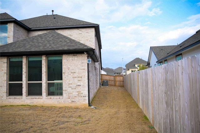 view of home's exterior with brick siding, a fenced backyard, a lawn, and roof with shingles