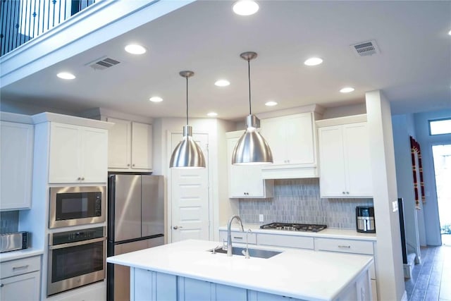 kitchen featuring a sink, light countertops, appliances with stainless steel finishes, decorative backsplash, and an island with sink