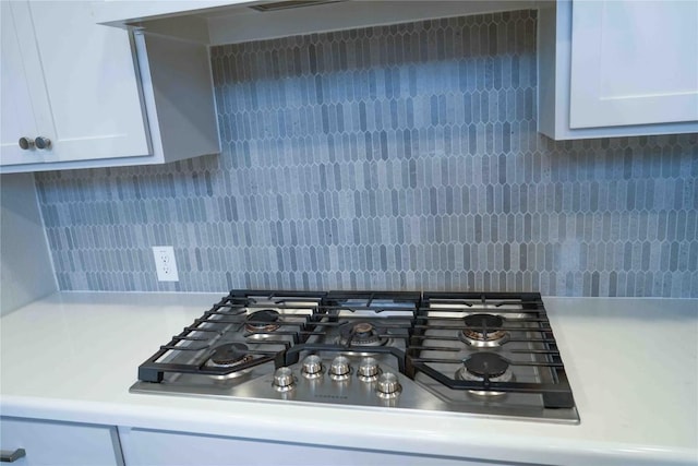 interior details with stainless steel gas cooktop, light countertops, tasteful backsplash, and white cabinetry