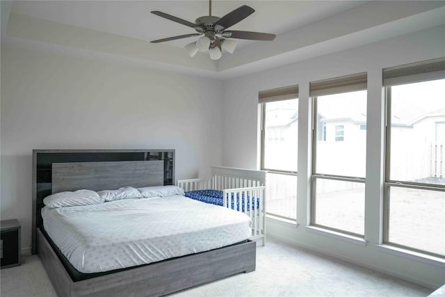 bedroom with a raised ceiling, light colored carpet, ceiling fan, and baseboards