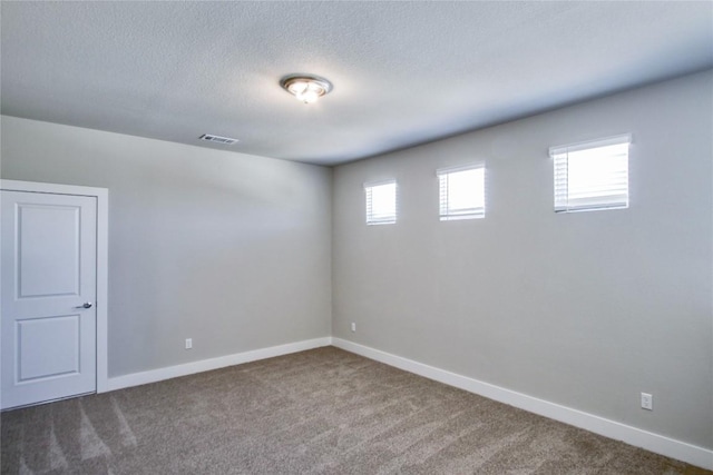 carpeted spare room with a textured ceiling, visible vents, and baseboards