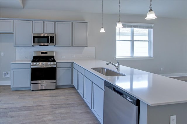 kitchen with light countertops, appliances with stainless steel finishes, a sink, light wood-type flooring, and a peninsula