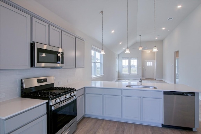 kitchen with a peninsula, a sink, light countertops, appliances with stainless steel finishes, and light wood-type flooring